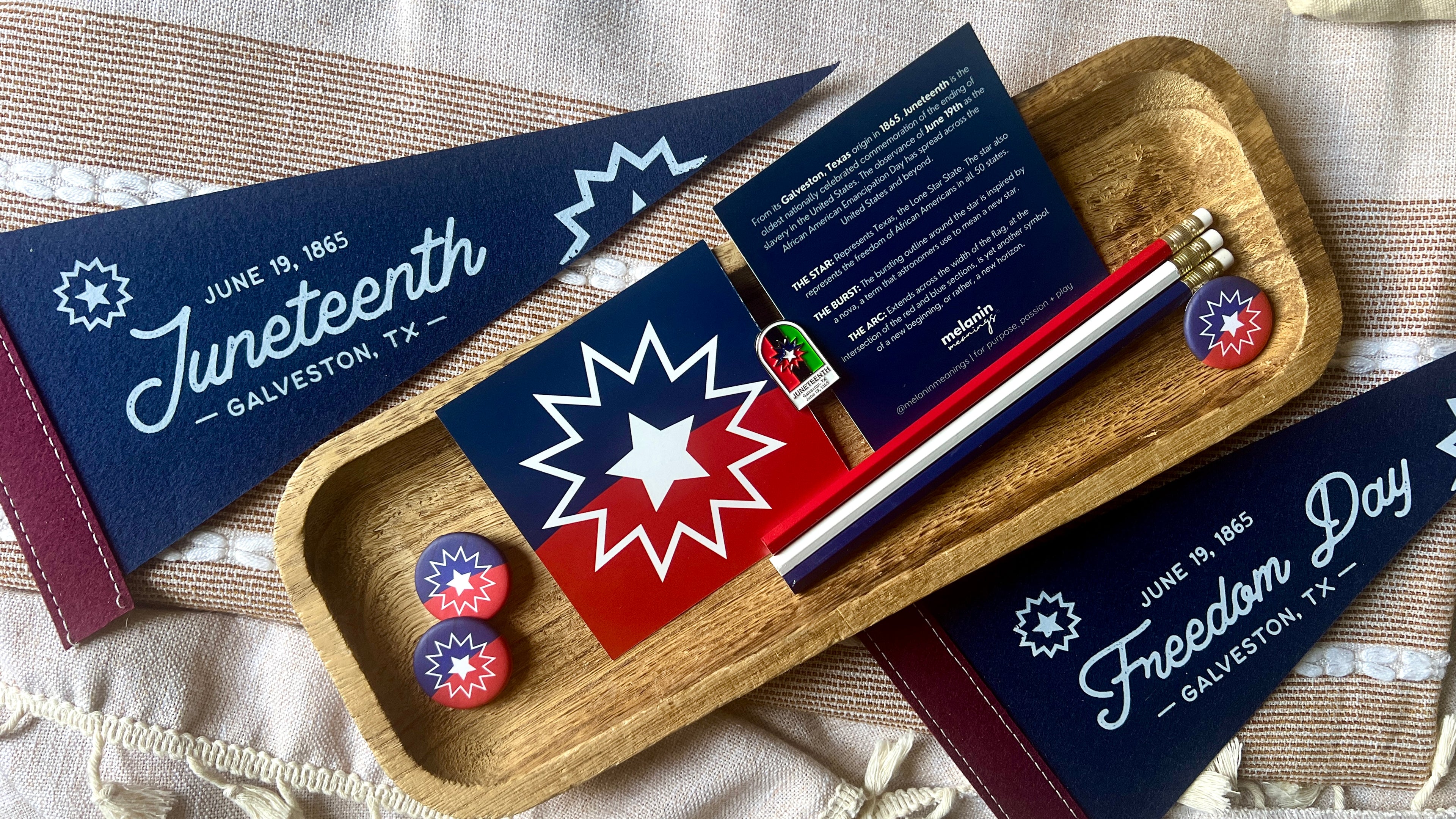 Collection of Juneteenth-themed items including flags, cards, and pins on a wooden tray.